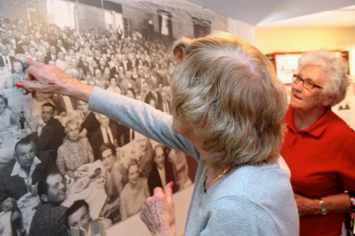 Irene Pendzick, left, and Dottie Krukowski look for familiar faces in the mural-size photo of a large gathering at Polish Hall in 1959. 