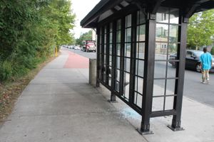 A pedestrian crosses Flanders Road in traffic last Tuesday afternoon, near the McDonald's restaurant. In the foreground is a county bus shelter which has had one of its glass panels broken. A heap of broken safety glass lies on the sidewalk inside the shelter.