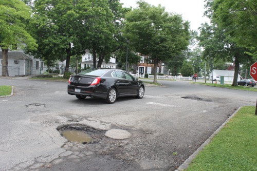 A car moves out of its lane of travel to avoid potholes in the town's municipal lot north of East Main Street. Photo: Denise Civiletti